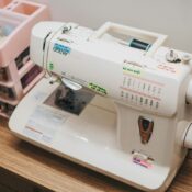 Dikiş makinesi üzerinde iplik yönü, iğne kaldırma, geri dikiş ve dikiş ayar sembolleri ile kullanım rehberi.